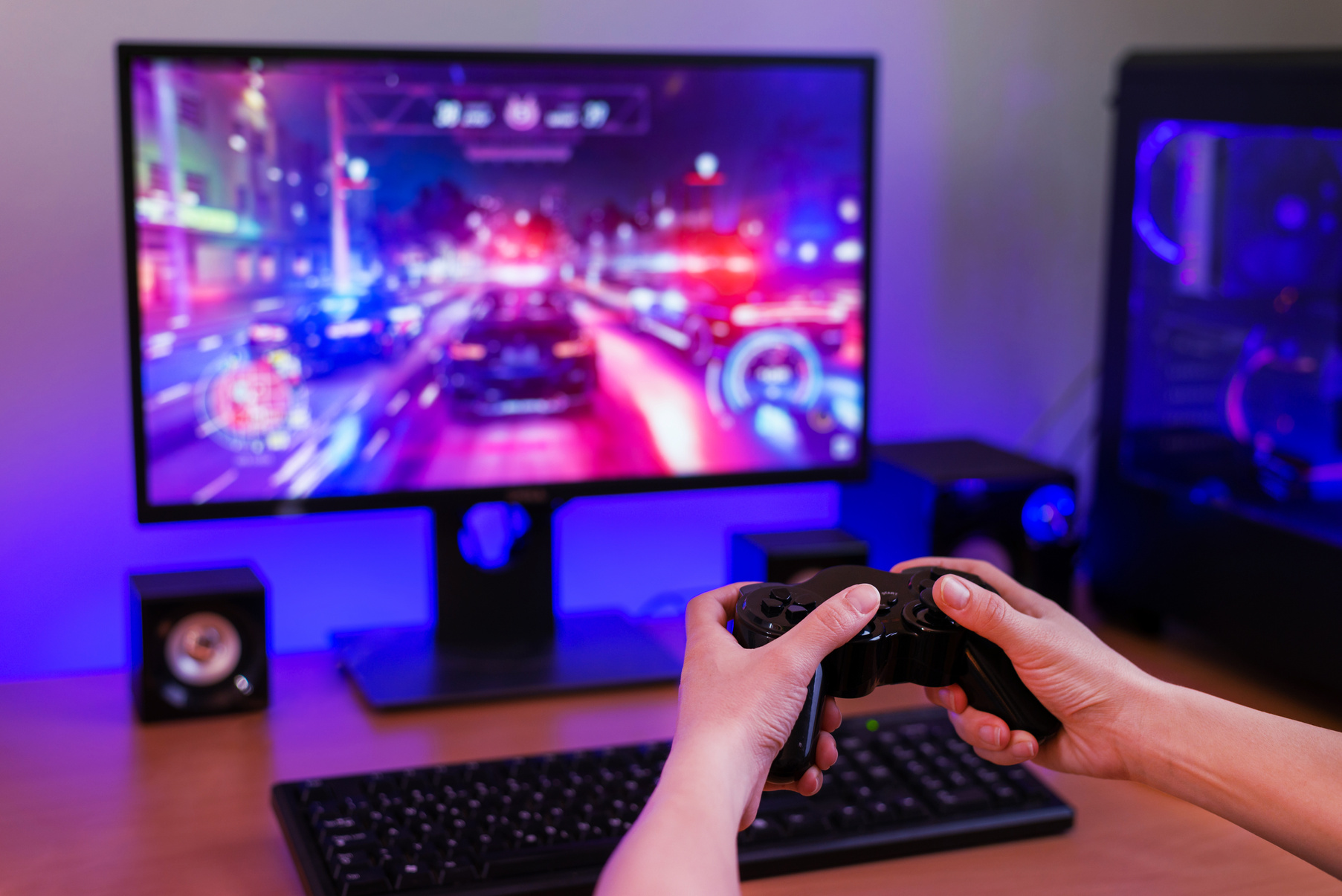 Playing racing games on computer concept. Hand holds the joystick. In the background is a gaming computer with RGB light.